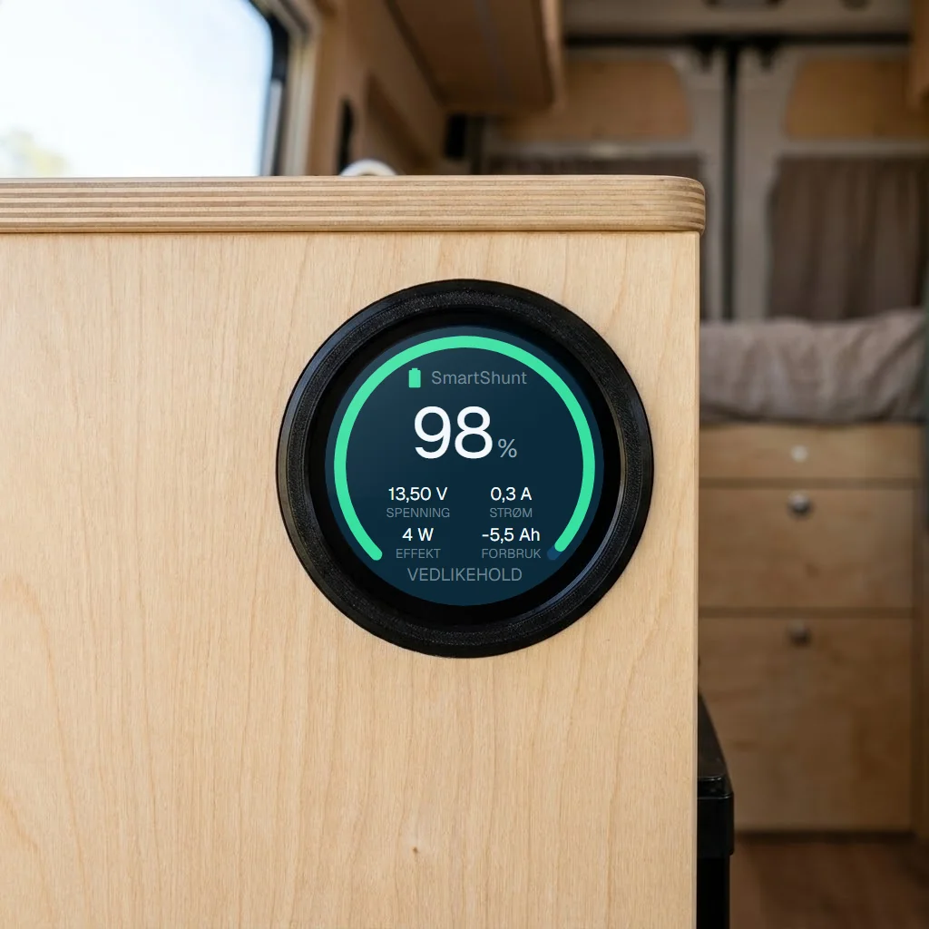 Voltvik-enheten felt inn i en finerfront i en campervan, med batterisiden på skjermen: 98 %, 13,50 V, 0,3 A og statusen VEDLIKEHOLD